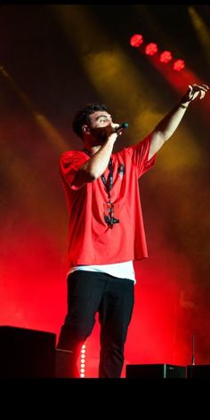 a man standing on top of a stage holding a microphone in his right hand and wearing a red shirt