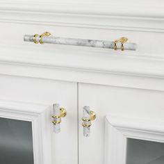 a white cabinet with gold handles and marble door knobs on the front, along with two glass doors