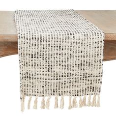 a white and black table runner with tassels on it's ends, sitting on a wooden bench