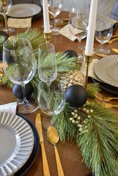 the table is set for christmas dinner with silverware and pine cones on it, along with candles