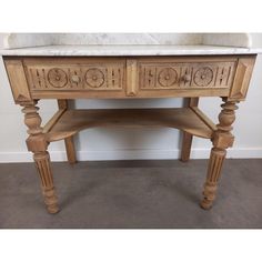 a wooden table with marble top and two drawers on one side, in front of a white wall