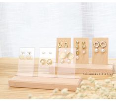 four pairs of earrings are displayed on wooden stand with flowers in the background and white curtain behind them