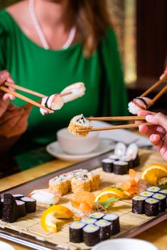 people eating sushi and chopsticks at a table with other foods on it