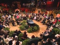 a large group of people sitting in front of a stage with a piano on it