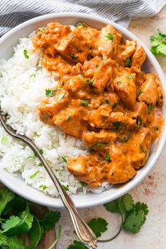 a white bowl filled with rice and meat covered in sauce next to cilantro