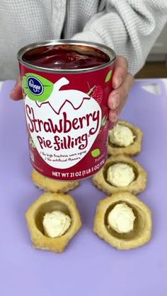 a person holding a can of strawberry pie filling on top of some crackers with cream cheese in the middle