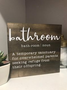 a bathroom sign sitting on top of a white counter next to a potted plant