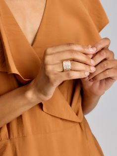 a woman in an orange dress is holding her hands together and wearing a gold ring