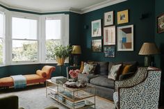 a living room filled with furniture and paintings on the wall next to two large windows