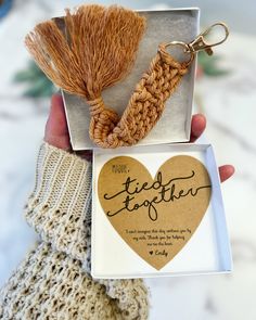 a person holding two small boxes with tassels on them and a heart shaped keychain