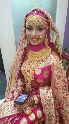 a woman in a pink and gold bridal outfit holding a cell phone while sitting on a chair