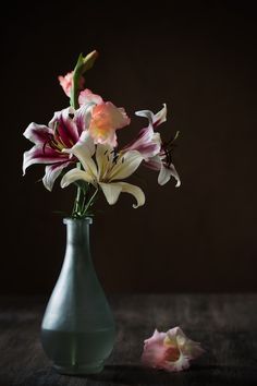 a vase filled with pink and white flowers on top of a wooden table in front of a dark background