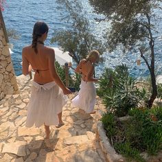 two women in white bathing suits walking up steps to the beach with trees and water behind them