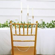 a wooden chair sitting next to a white table covered in greenery and candles on top of it