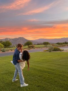 a man holding a woman in his arms while the sun is setting behind them and there are mountains in the distance