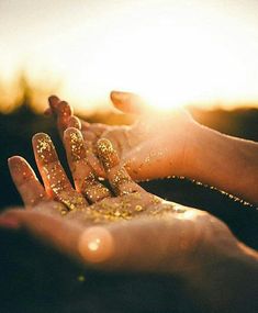 two hands with gold glitter on them holding each other's hand in front of the sun