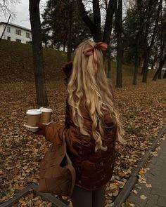 a woman with long blonde hair holding a cup of coffee in her hand and wearing a brown jacket