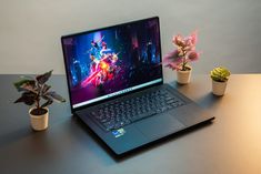 an open laptop computer sitting on top of a table next to potted plants and cacti