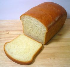 a loaf of white bread sitting on top of a wooden table next to a slice of bread