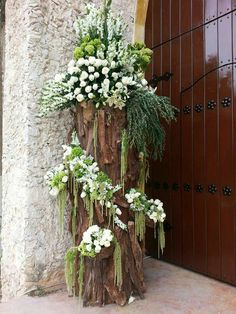 a tall tree trunk with flowers and greenery on it in front of a door