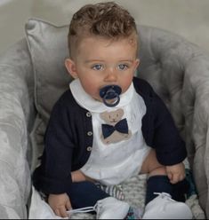 a baby sitting in a chair with a pacifier in his mouth and wearing a bow tie