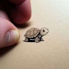 a hand holding a small sticker with a drawing of a turtle on it