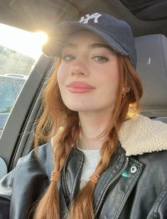 a woman sitting in the back seat of a car wearing a baseball cap and braided hair