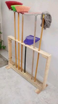 three brooms and two mop's on a wooden rack in front of a white wall