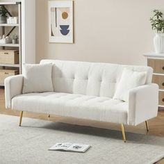 a white couch sitting on top of a wooden floor next to a book shelf filled with books