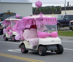 two pink golf carts are driving down the street with balloons on them and some people sitting in the back