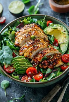 a salad with chicken, avocado, tomatoes and spinach in it on a table