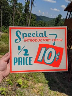 a hand holding up a sign advertising an item for sale in front of some trees