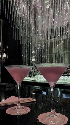 two martinis sitting on top of a black table under a crystal chandelier