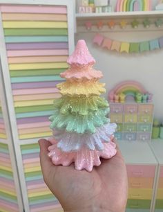 a hand holding a small toy christmas tree in front of a rainbow striped wallpaper