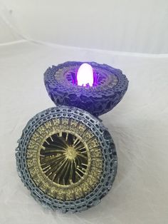 two decorative objects sitting on top of a white tablecloth covered surface, one is purple and the other is gold