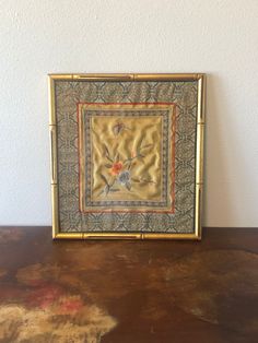 a gold frame with an embroidered design on it sitting on top of a wooden table