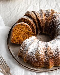 a bundt cake with powdered sugar on top sits on a plate next to a fork