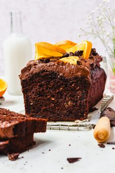 a chocolate cake with orange slices on a cooling rack next to some milk and flowers