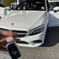 a person holding a car key in front of a white mercedes