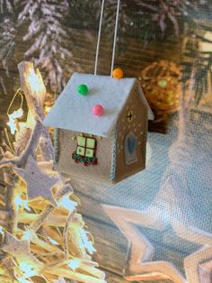 a small house ornament hanging from a christmas tree with lights on it's roof