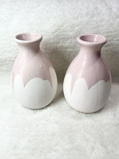 two pink and white vases sitting side by side on a white carpeted surface