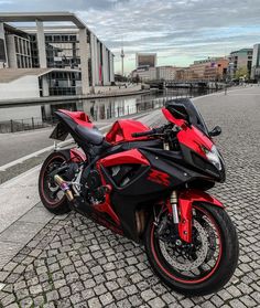 a red and black motorcycle parked on the side of a road next to a body of water