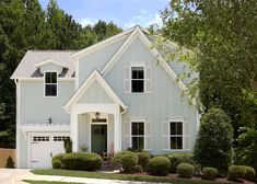 a blue house with white trim and two story windows on the front, surrounded by trees