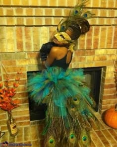 a woman in a peacock costume standing next to a fire place with feathers on it