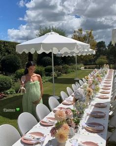 a woman standing next to a long table with plates and flowers on it in front of an umbrella