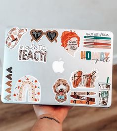 a person holding up a laptop with stickers on it