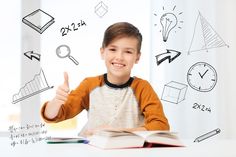 a young boy sitting at a table with an open book and thumbs up in front of him