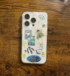 an iphone case with stickers on it sitting on top of a wooden table next to a cell phone