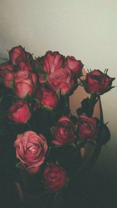 a vase filled with lots of red roses on top of a wooden table next to a white wall