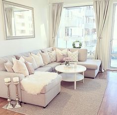 a living room filled with furniture next to a large window covered in white blankets and pillows